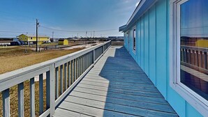 A wooden deck with a railing, a clear sky, and a building with a blue exterior. - Aransas Bay Getaway by Miss Kitty’s (Rockport)