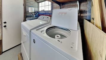 A laundry room with a front-loading washer and dryer, a window, and a shelf with cleaning supplies.