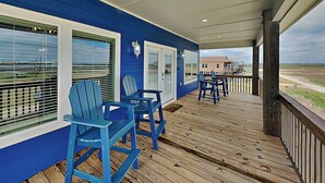 A covered deck with blue Adirondack chairs, a table, and a view of the beach. - Fish Tales by Miss Kitty’s (Rockport)