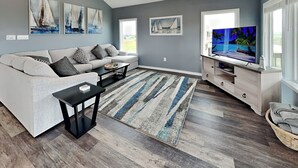 A modern living room with a grey sofa, a coffee table, and a TV on a wooden stand. - Fish Tales by Miss Kitty’s (Rockport)