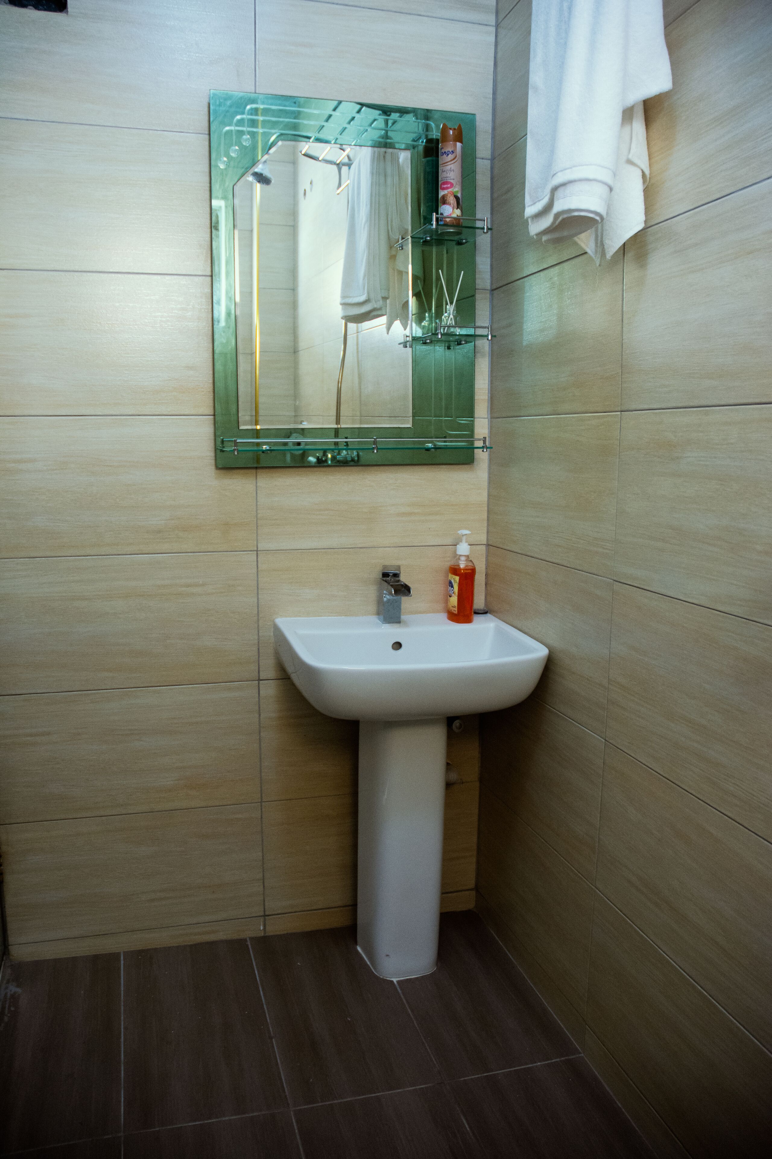 A bathroom with a white sink, a green-framed mirror, and a towel hanging on the wall.