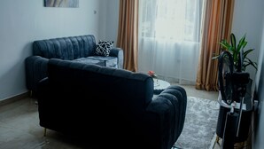 Ein Wohnzimmer mit einem dunkelblauen Sofa, einem kleinen Beistelltisch, einer Topfpflanze und einer TV-Konsole mit einem Ventilator.