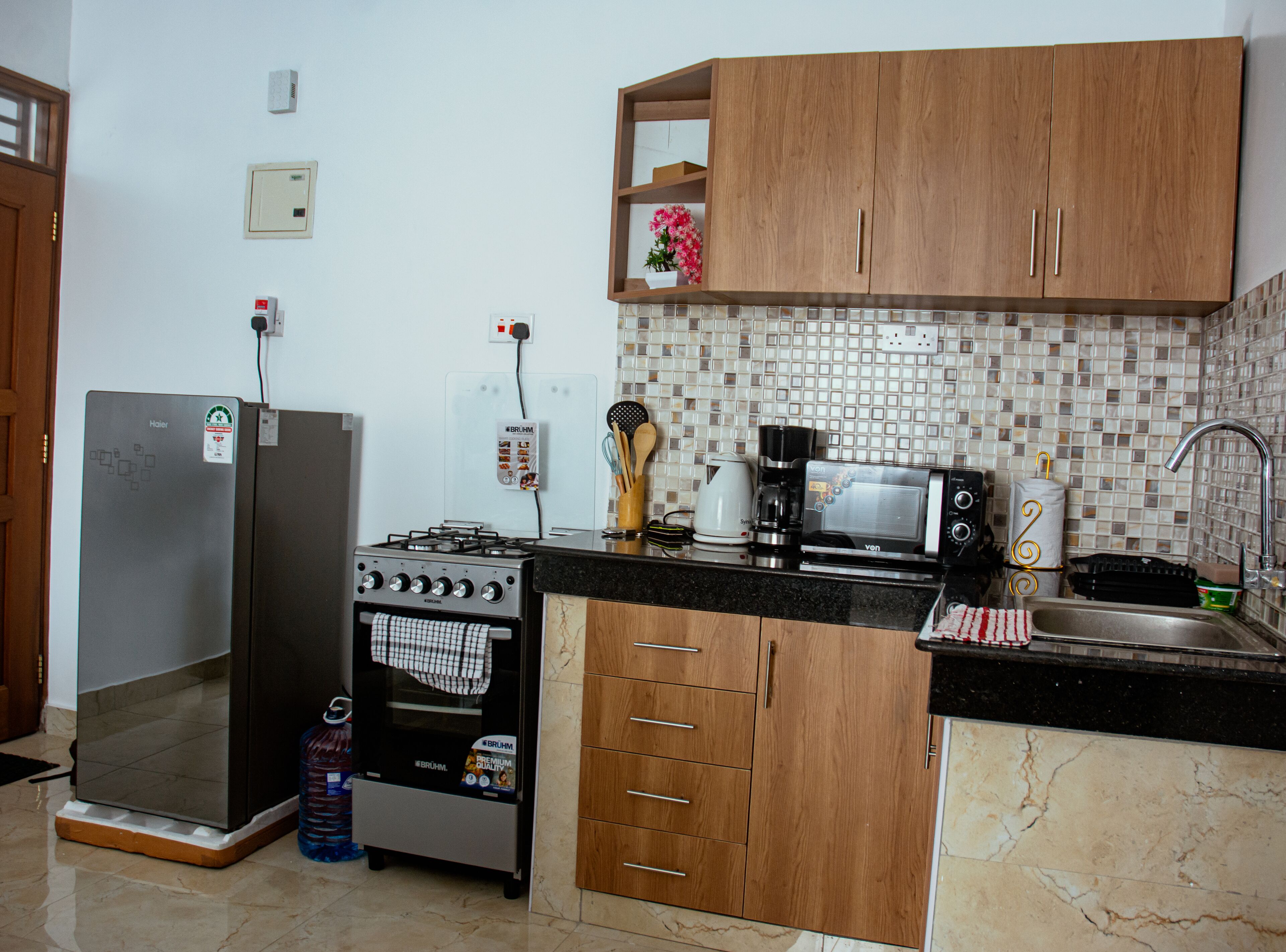 Une cuisine de taille réduite, équipée d’une cuisinière à gaz, d’un four à micro-ondes et de meubles de rangement en bois.