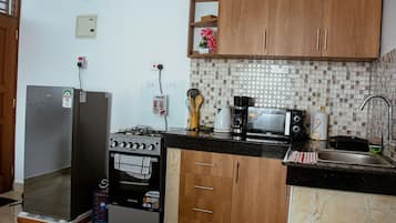 Une cuisine de taille réduite, équipée d’une cuisinière à gaz, d’un four à micro-ondes et de meubles de rangement en bois.