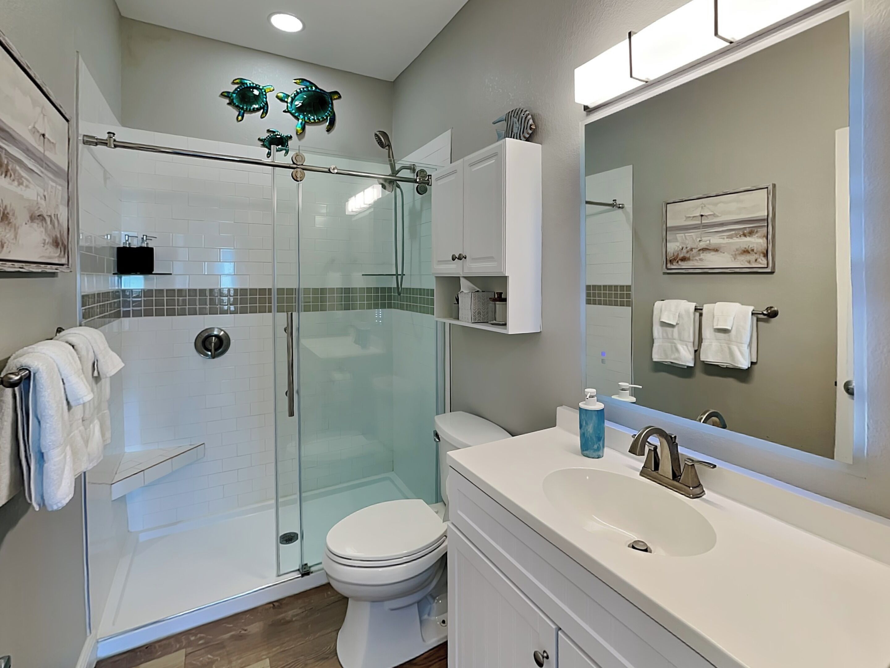 A modern bathroom with a glass-enclosed shower, a white toilet, a sink with a mirror, and a towel rack.