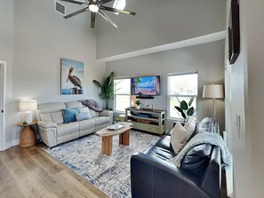 A living room with a sofa, coffee table, TV, and a ceiling fan. - Inn at Pelican Paradise by Miss Kitty’s (Rockport)