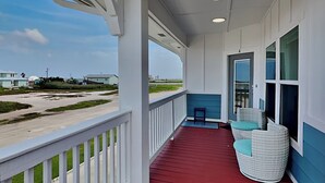 A covered porch with a red floor, white railings, and a view of a beach and houses.