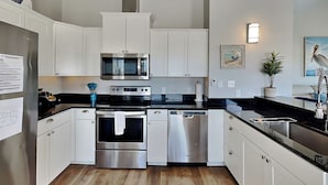 A modern kitchen with white cabinetry, stainless steel appliances, and a wooden floor.