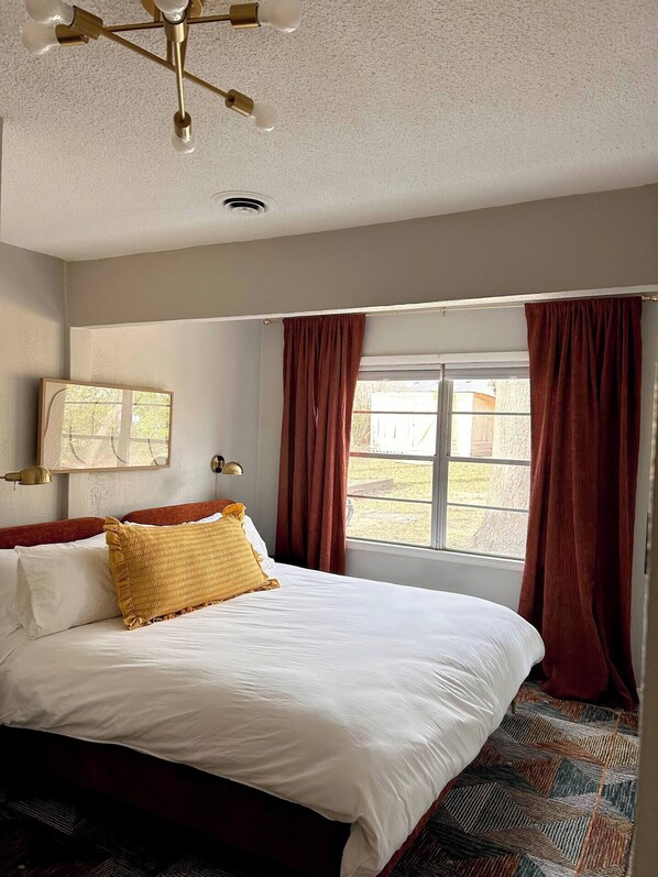 Un dormitorio con una cama grande, una ventana con cortinas, un ventilador de techo y una lámpara de pared.