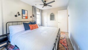 A bedroom with a bed, a ceiling fan, a nightstand, a wall-mounted lamp, and a door with a mirror.