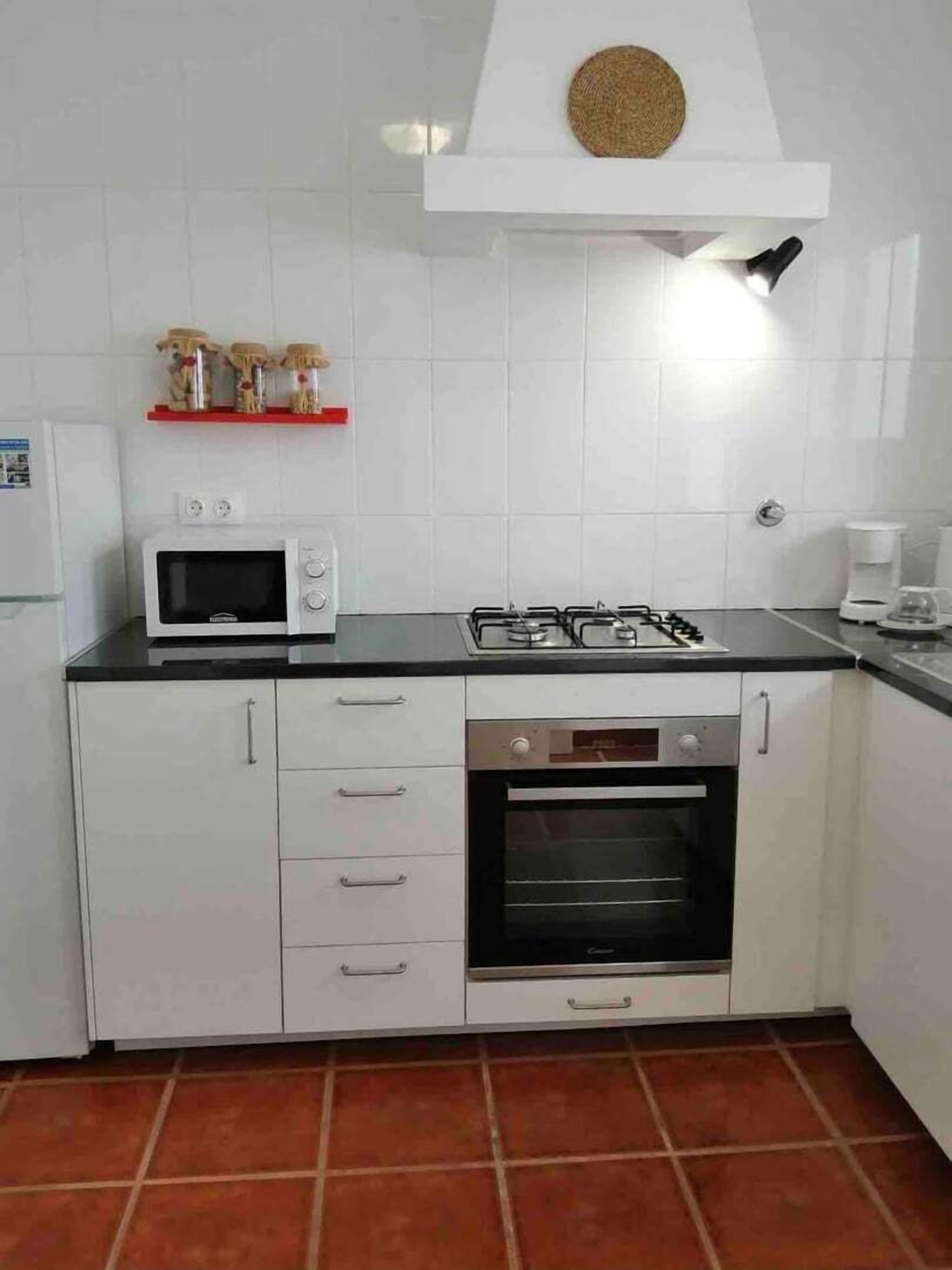 Una cocina compacta con armarios blancos, microondas, estufa a gas y horno.