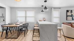 Una cocina moderna con una isla de mármol, taburetes negros y lámparas colgantes.
