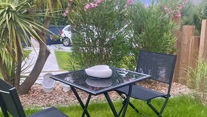 Une petite terrasse extérieure avec une table à plateau en verre, deux chaises noires et un bol blanc.
