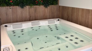 Un bain à remous doté de plusieurs jets, d’un panneau de commande et d’un mur en bois orné de feuillage vert et de fleurs rouges.