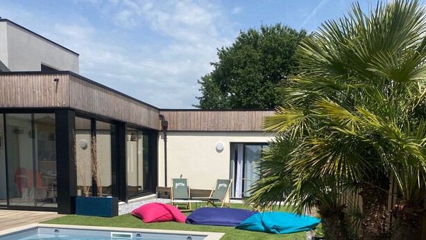Une piscine bordée de gazon synthétique, avec des chaises longues et un bâtiment moderne doté de grandes fenêtres.