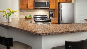 A kitchen with granite countertops, a stainless steel refrigerator, a microwave, a stove, and wooden cabinets. - 2-bedroom condo in marvelous Palm Desert with AC, WiFi, fitness room (Palm Desert)