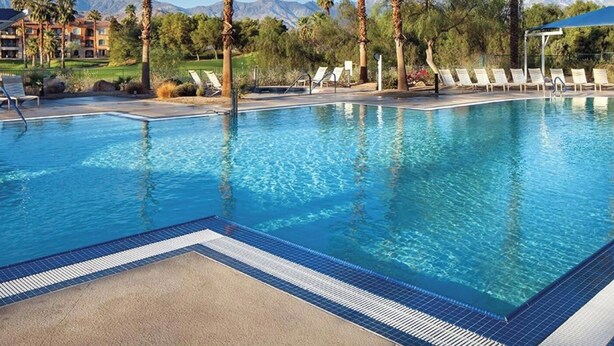 A clear swimming pool with lounge chairs and umbrellas, surrounded by palm trees and a mountainous backdrop. - 2-bedroom condo in marvelous Palm Desert with AC, WiFi, fitness room (Palm Desert)