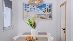 A dining area with a white table, a woven light fixture, a view of the beach through a window, and a vase with plants. - GuestReady - Sea Escape Azores (Lagoa)