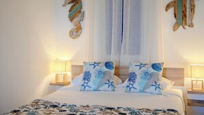 A neatly made bed with a floral bedspread, two pillows with starfish designs, and a wall-mounted decorative piece resembling a sea shell. - GuestReady - Sea Escape Azores (Lagoa)