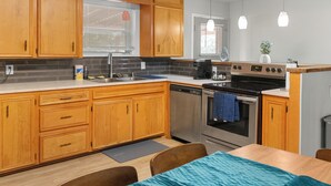 A modern kitchen with wooden cabinets, a stainless steel sink, a stove, and a dishwasher. - Modern 4 Bedroom with King bed (Lubbock)