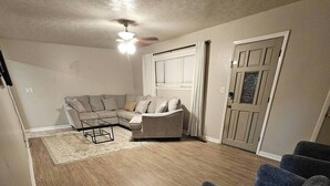 A living room with a sectional sofa, a coffee table, and a dark-colored armchair. - Modern 4 Bedroom with King bed (Lubbock)