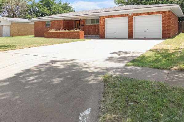 A two-story brick house with a front garage, a covered driveway, and a well-maintained lawn.