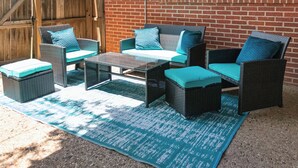 A patio area with wicker furniture, including chairs and a table, set against a brick wall. - Modern 4 Bedroom with King bed (Lubbock)