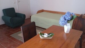 A small room with a green sofa, a wooden table with a vase of flowers, and a wooden chair. - GuestReady - Azores City Loft (Ponta Delgada)