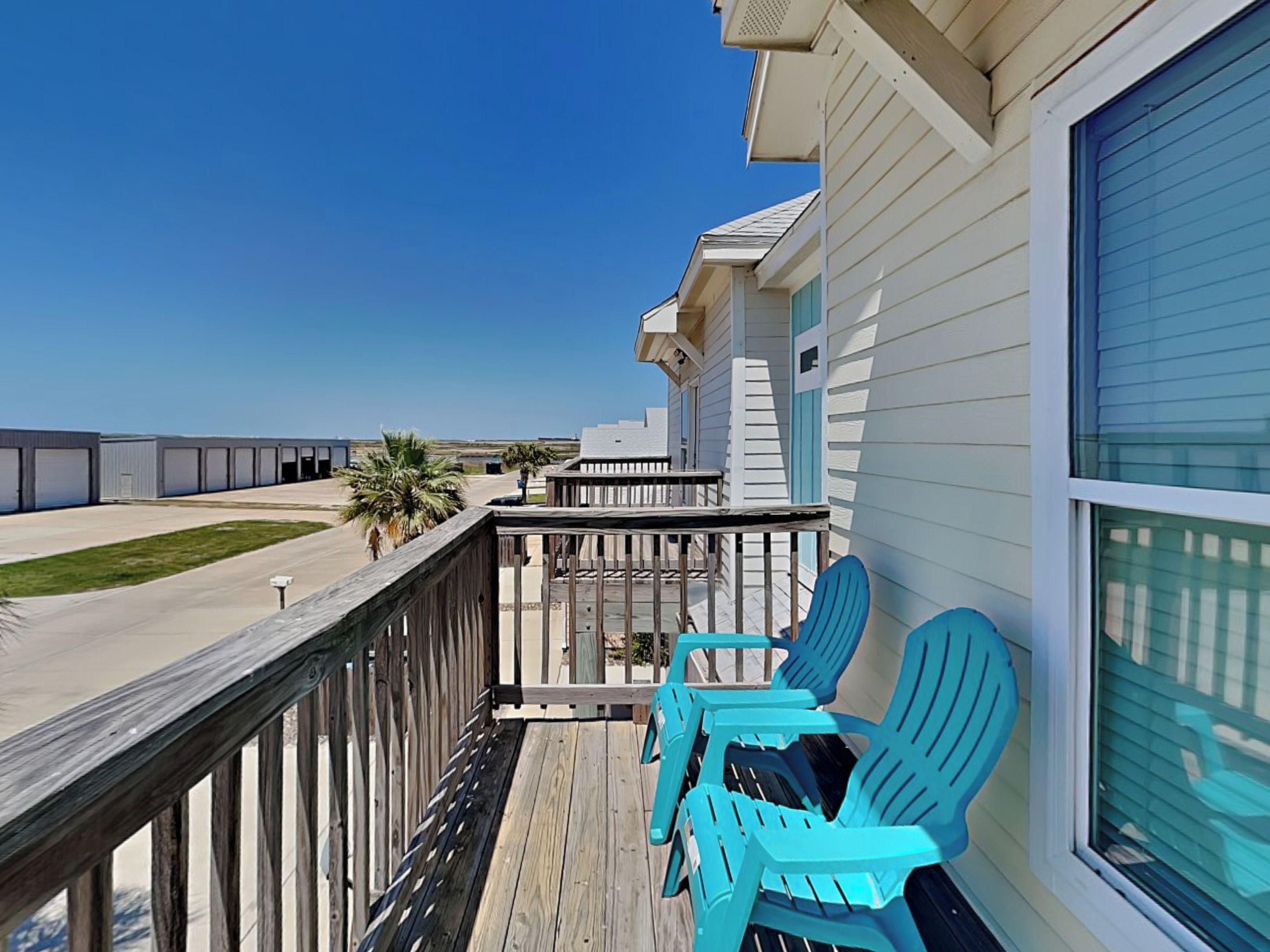 A wooden deck with turquoise chairs, a clear view of a parking lot, and a building with large windows.