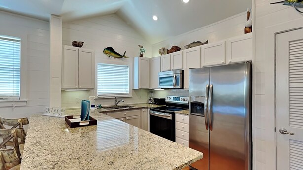 A modern kitchen with white cabinets, a stainless steel refrigerator, a microwave, and a granite countertop.