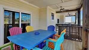 A covered patio with a blue table and colorful chairs, a ceiling fan, and a view of the backyard.