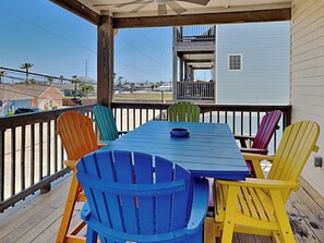 A covered outdoor deck with a blue table and colorful Adirondack chairs. - Reel Nauti by Silver Sands Vacation Rentals (Port Aransas)
