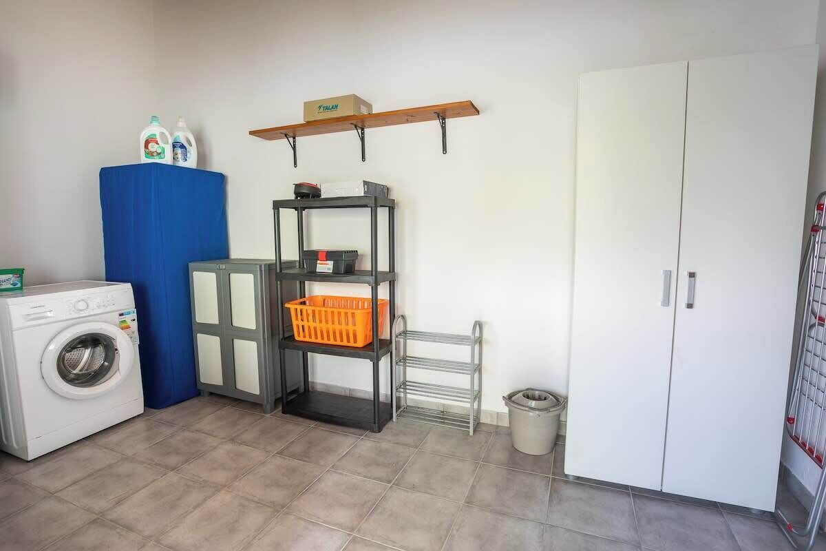 Uma área de lavanderia com máquina de lavar, cesto de roupa azul, estante de metal e guarda-roupa branco.
