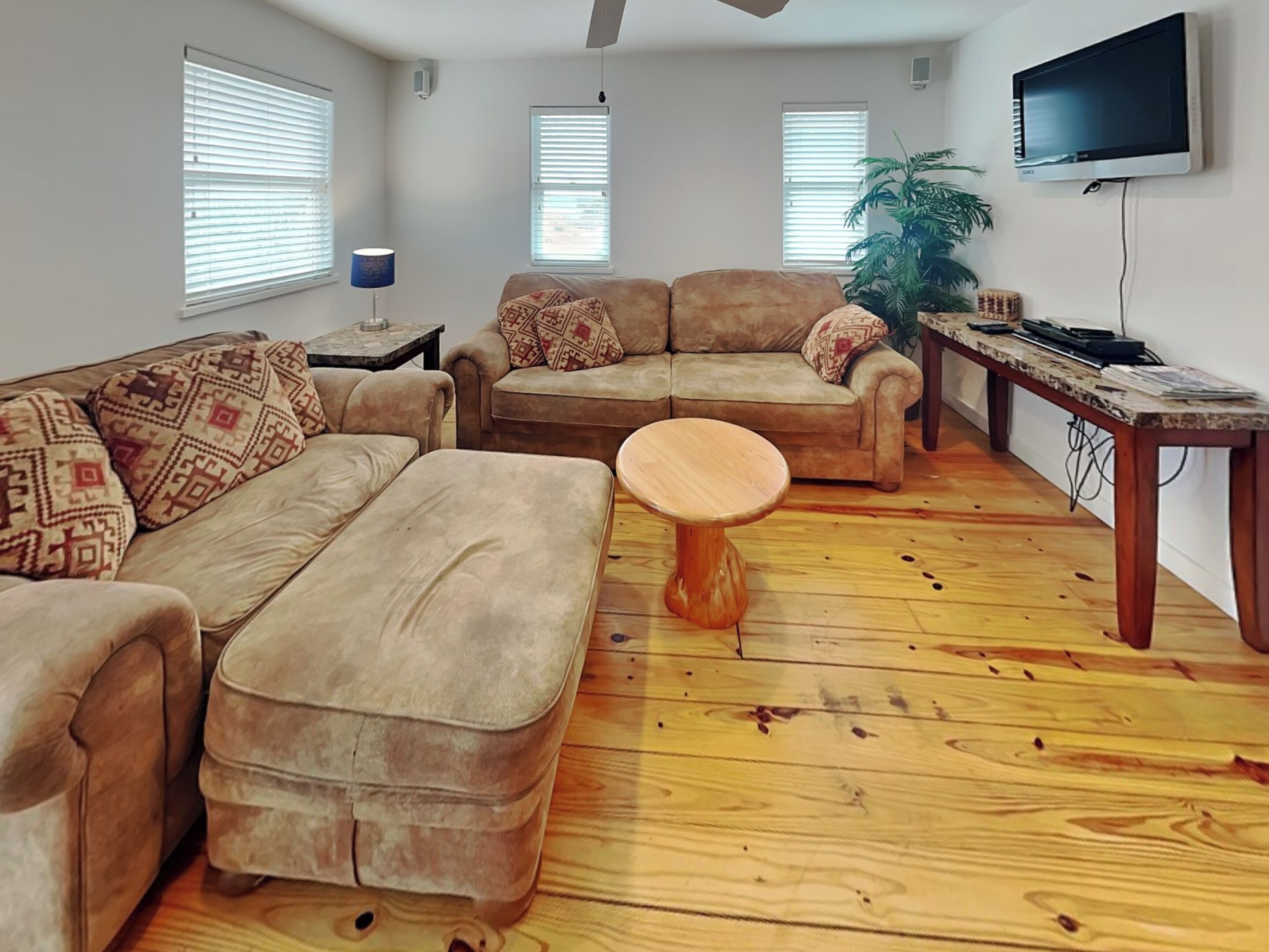 A living room with a sofa set, a wooden coffee table, and a TV mounted on the wall.