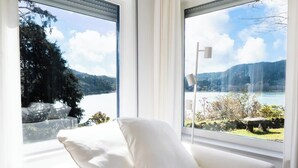 A white sofa with a view of a lake and mountains through large windows.