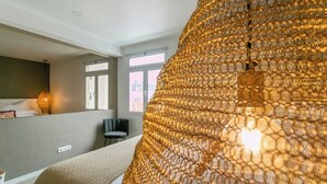 A hotel room with a large window, a bed with a beige cover, and a hanging light fixture.