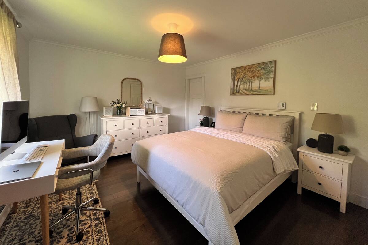 A hotel room with a bed, desk, chair, dresser, and bedside tables.