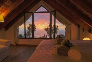 A bedroom with a large window overlooking the sea, a bed with rolled towels, and wooden beams. - GuestReady - Green OceanView Relaxing Cottage (Ponta Delgada)