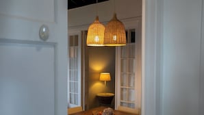 A dining area with a wooden table, two wicker pendant lights, and a lamp on a side table. - GuestReady OceanFront Casa do Mirante (Ponta Delgada)