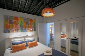 A hotel room with a bed, a large abstract painting, a hanging lamp, and a wardrobe with a mirror.
