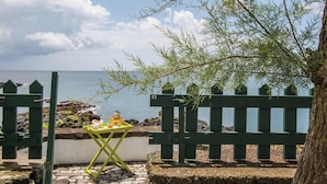 A coastal view with a wooden fence, a table with fruits, and a tree. - GuestReady OceanFront Casa do Mirante (Ponta Delgada)