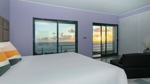A bedroom with a large bed, two sliding glass doors leading to a balcony with a sunset view. - GuestReady - Sunset House (Relva)