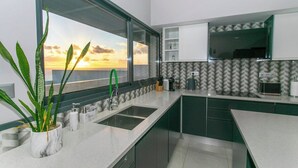 A modern kitchen with a large window, green cabinets, and a marble countertop. - GuestReady - Sunset House (Relva)