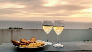 A table with a plate of cheese and crackers, two glasses of white wine, and a view of the ocean at sunset. - GuestReady - Sunset House (Relva)