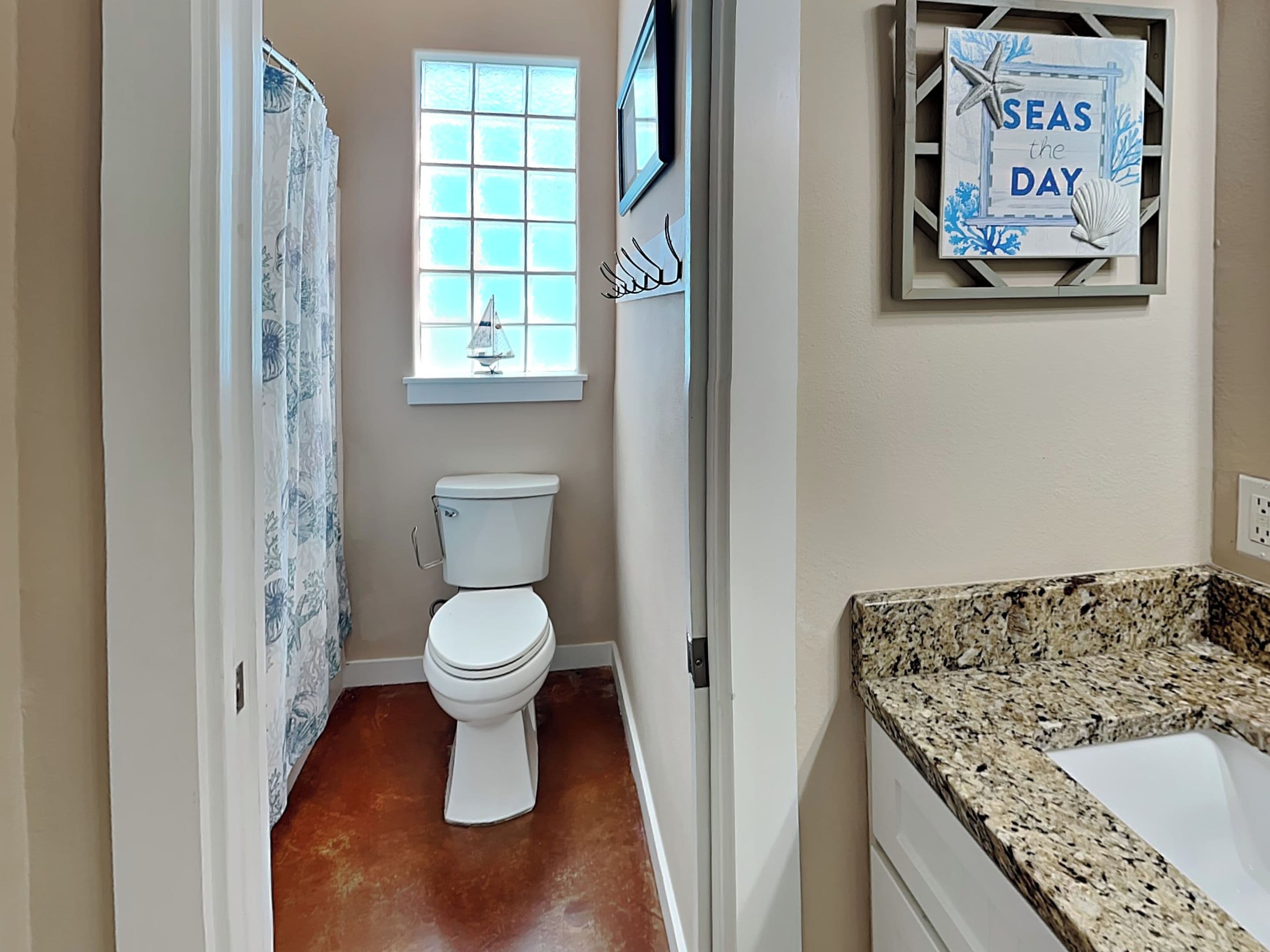 A bathroom with a toilet, a window with a view, and a granite countertop.