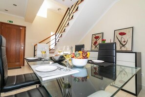 A modern dining area with a glass table, black leather chairs, and a fruit bowl. - GuestReady - Casa do Parque (Ponta Delgada)