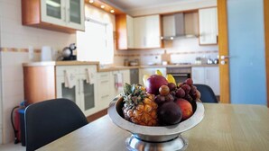 A kitchen with wooden cabinets, a stainless steel bowl of fruit on a table, and a window providing natural light. - GuestReady - Casa do Parque (Ponta Delgada)