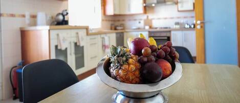 A kitchen with wooden cabinets, a stainless steel bowl of fruit on a table, and a window providing natural light.