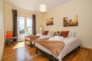 A hotel room with two beds, a window with curtains, a chair, and artwork on the walls. - GuestReady - Casa do Parque (Ponta Delgada)