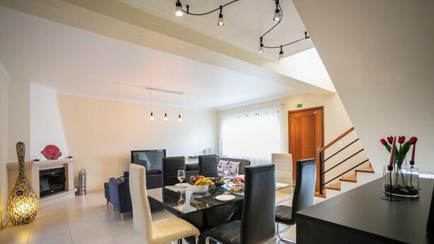 A modern living room with a dining area, a fireplace, and a staircase. - GuestReady - Casa do Parque (Ponta Delgada)
